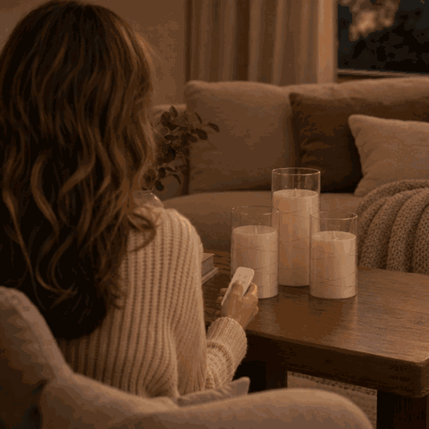 Woman switches on the LED candle set with the remote control from the sofa