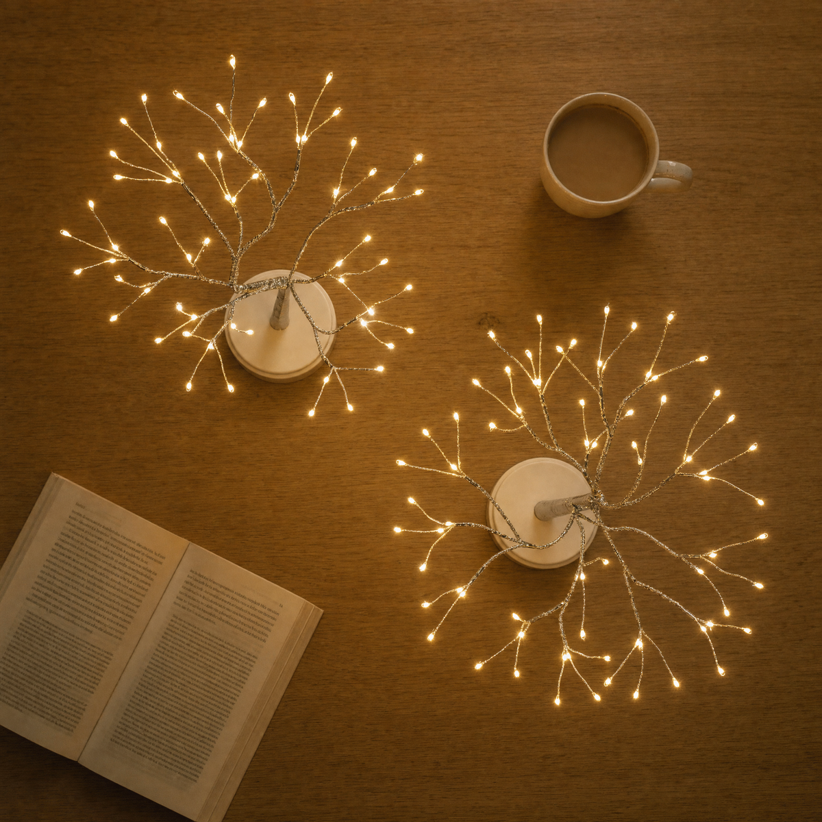 Two LED light trees from above on a wooden table with a book and a cup